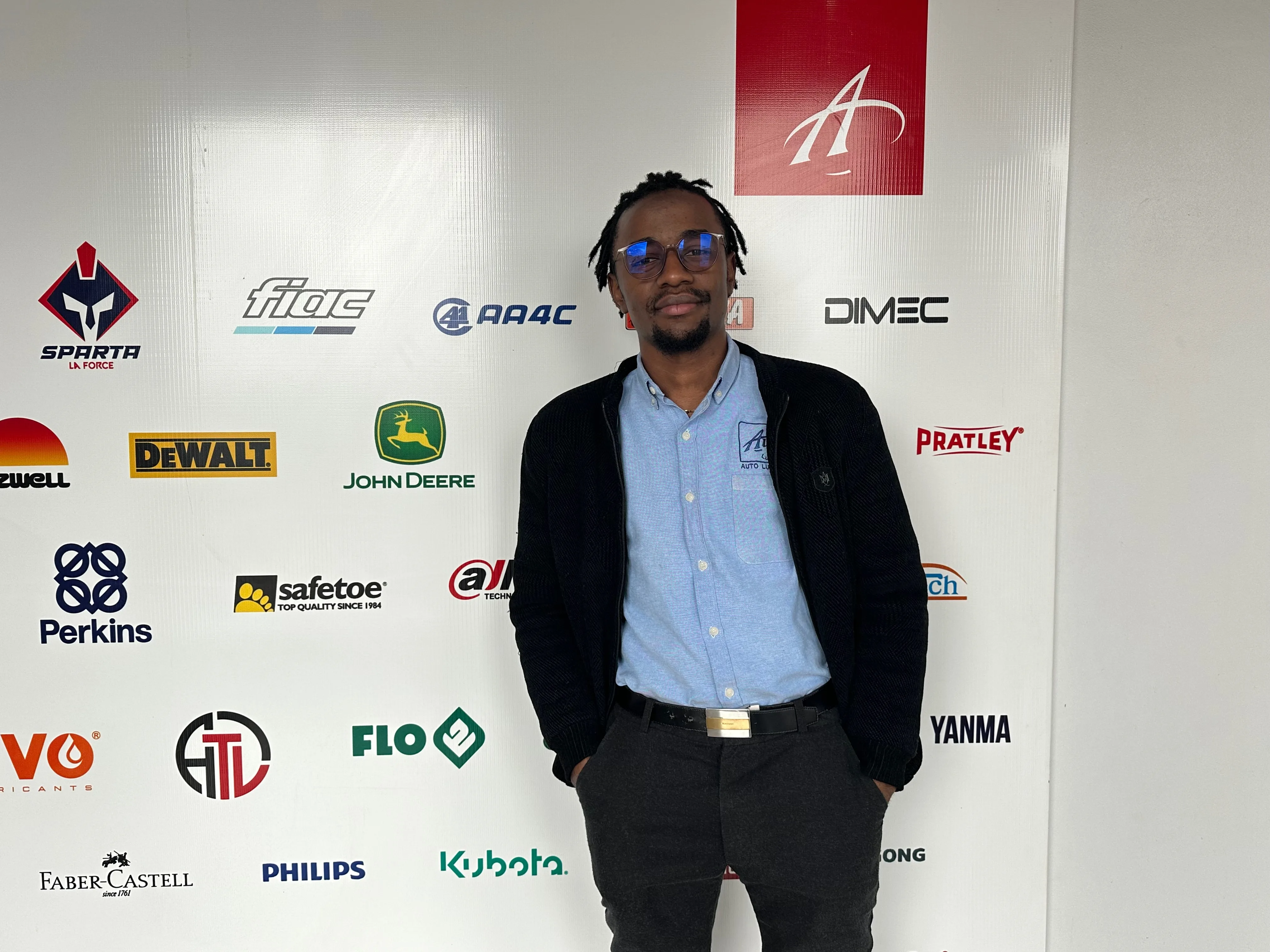 Bernard at Auto Lubumbashi in front of partner logos